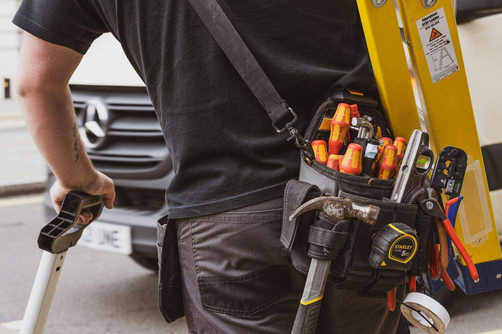Service technician carrying a ladder and full tool belt on a job