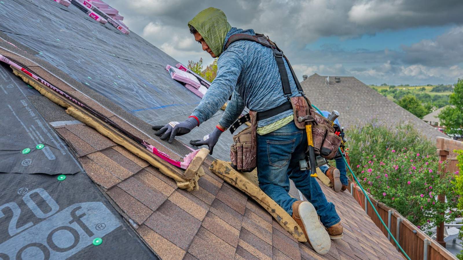 Roofer installing shingles on a residential roof with storm clouds overhead