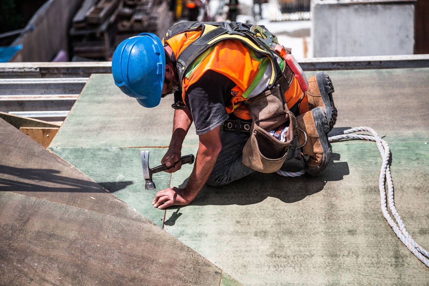 Roofer in a hard hat and harness nailing down roof decking