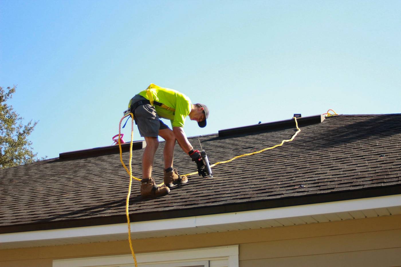 Roofer in a safety harness sealing shingles on a residential roof
